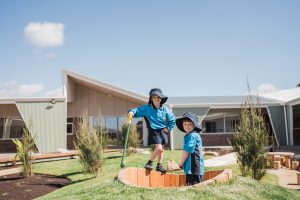 Image of two children playing in a sandpit in front of the school building
